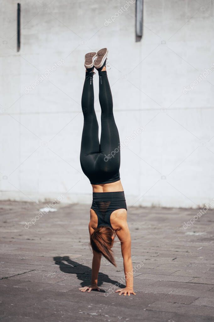 Powerful girl doing advance acrobat skills in the city. Urban background . Vertical photo. 