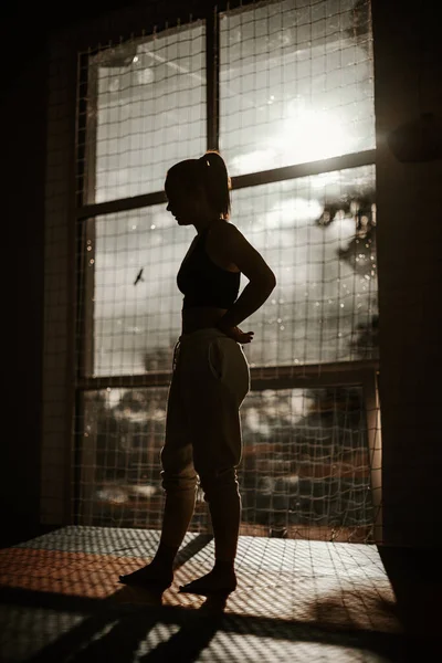 Silhouette av en kvinne som sto i gymsalen ved solnedgang. kvinnen har hendene på hoftene – stockfoto