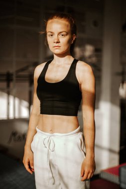 Portre. Genç ve çekici bir kadın kameraya ciddi ciddi bakıyor. Spor salonunda spor kıyafetleri içinde bir sporcu. gün batımı