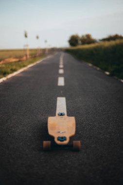 Yolun ortasında bir figür olmadan uzun bir tahta. Boşluğu kopyala. Dikey afiş. Poster. Longboard günü posteri.