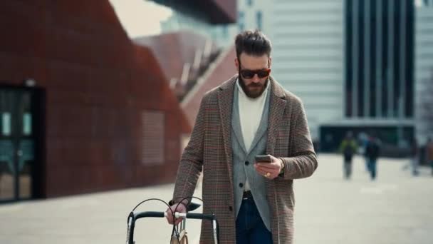 Giovane con bicicletta che tiene uno smartphone davanti all'edificio. Uomo d'affari creativo in una moderna area di business. — Video Stock