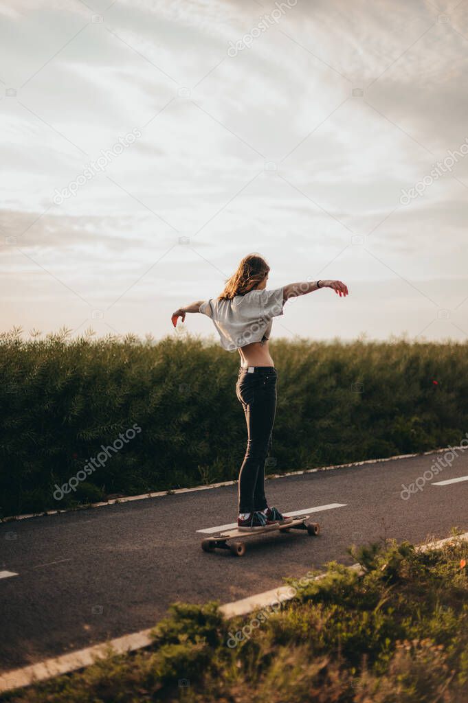Girl rides a longboard with arms outstretched and enjoying a free ride. Sunny day , poster, longboard day vertical banner