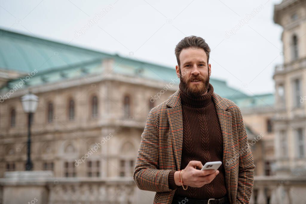Young man holding a smartphone front of building. Creative businessman in historical city area.
