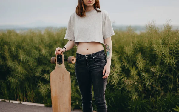 Pionowy plakat. Młoda kobieta bez twarzy trzymająca longboard w ręku. w tle jest zielony charakter — Zdjęcie stockowe