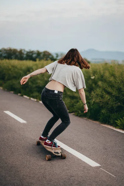 Bakvendt, kvinnelig skateboardkjører på sykkelstien, grønn eng i bakgrunnen. stockbilde
