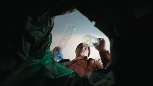 Mies heittää muovipullon roskakoriin. Alhaalta päin roskiksesta. Kierrätys ja saastuminen planeetan roskat — kuvapankkivalokuva