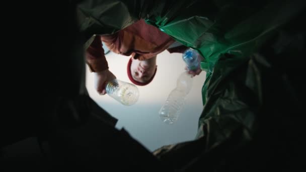 Un hombre tirando una botella de plástico en un cubo de basura. Vista inferior desde el cubo de basura. Reciclaje y contaminación del planeta con basura — Vídeos de Stock