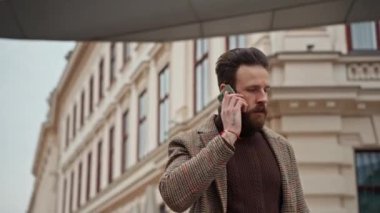 İş adamı şehirde bir cep telefonuyla yürüyor ve konuşuyor.
