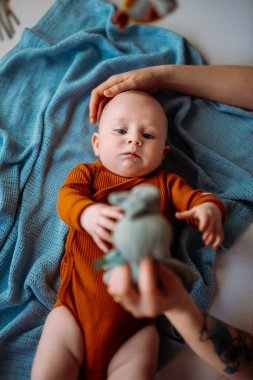  Anne mavi gözlü bebeğe bir oyuncak gösterir ve kafasını okşar.