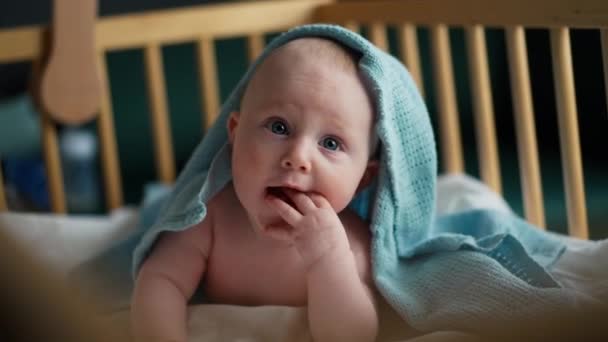 Egy kisbaba fekszik a kék takarón, mosolyog és szopogatja az ujjait. Kék szemű baba. — Stock videók