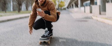 Orta bölüm afişi. Yakışıklı bir adam kaykay sürüyor ve akıllı telefonuna bakıyor.