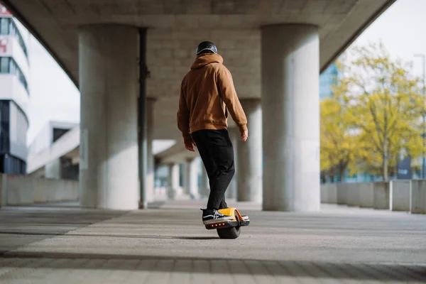 Young man in a helmet rides an electric skateboard. Onewheel rider in an urban background.