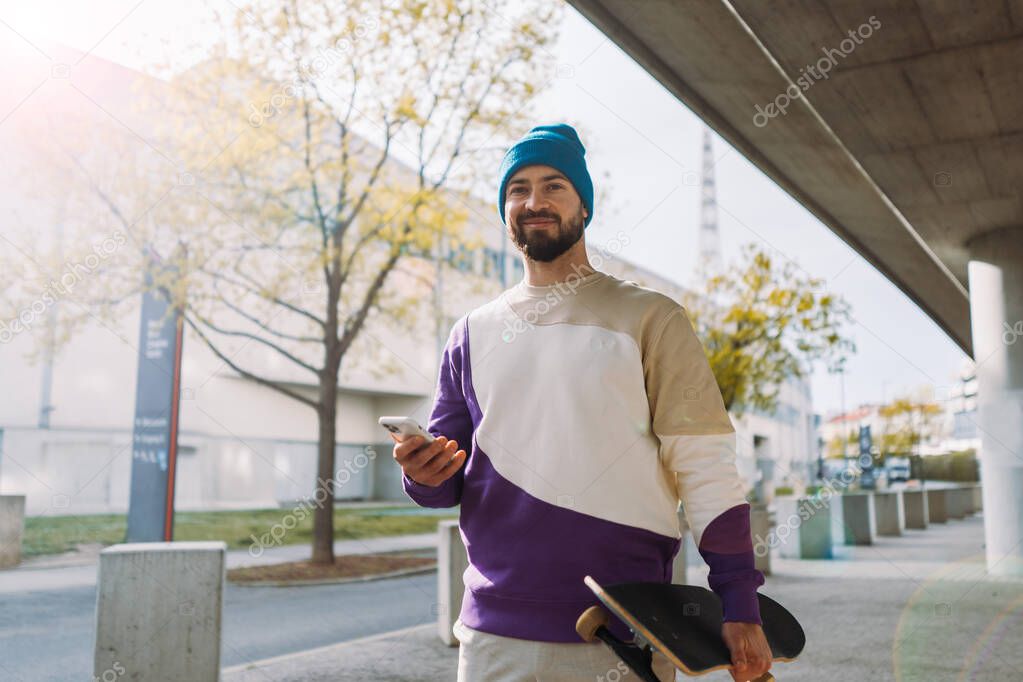 Portrait of stylish skater holds a skateboard in his hand and walks. man hold smartphone in hand.