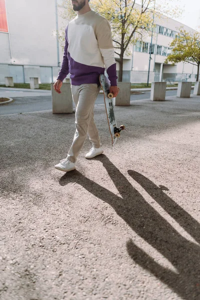 Μεσοτομή του σκέιτμπορντ. Κομψός άνετος άντρας που περπατάει στο δρόμο. Αστικό σημείο. Κάθετη φωτογραφία. — Φωτογραφία Αρχείου