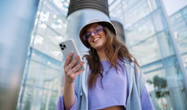 Genç havalı kız cep telefonunu tutuyor ve kullanıyor. Gülümseyen kadın arkadaşlarıyla mesajlaşıyor.