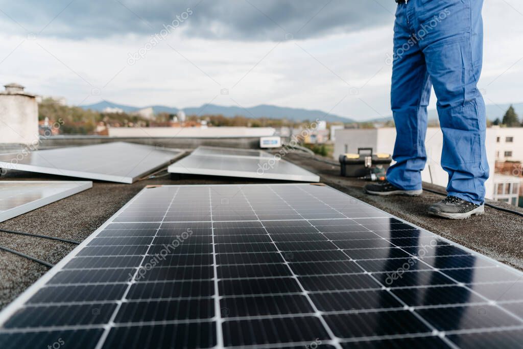 Close-up on the legs of a man standing by solar panels on the roof of a house Alternative energy. Cover photo