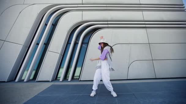 Modebewusste Frau mit Sonnenbrille und Hut, die draußen vor der Kamera tanzt. Tänzerin bei einer Tanzshow, die Freestyle-Stunts macht. Lustiges stylisches kaukasisches Hip-Hopgirl. 4K — Stockvideo