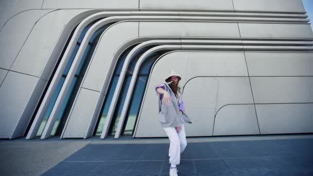 Modebewusste Frau mit Sonnenbrille und Hut, die draußen vor der Kamera tanzt. Tänzerin bei einer Tanzshow, die Freestyle-Stunts macht. Lustiges stylisches kaukasisches Hip-Hopgirl. 4K — Stockvideo