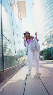 Spor giyimli modaya uygun beyaz kız dansçı sokak dansı hareketini sergiliyor. Dikey video. Neşeli yaz kadın sanatçısı şehirde koreografi gösterisi yapıyor..