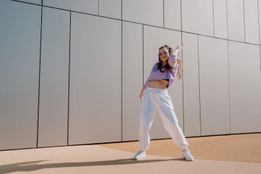 Cool young woman dancing with mobile. Urban futuristic background. Model posing 