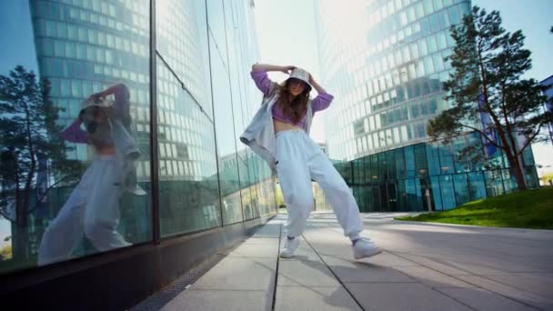 Modische flippige kaukasische Tänzerin in Sportbekleidung führt Streetdance-Bewegungen im Freien aus. Zeitlupenvideo. Fröhliche Sommerkünstlerinnen zeigen Choreografie in der Stadt. — Stockvideo