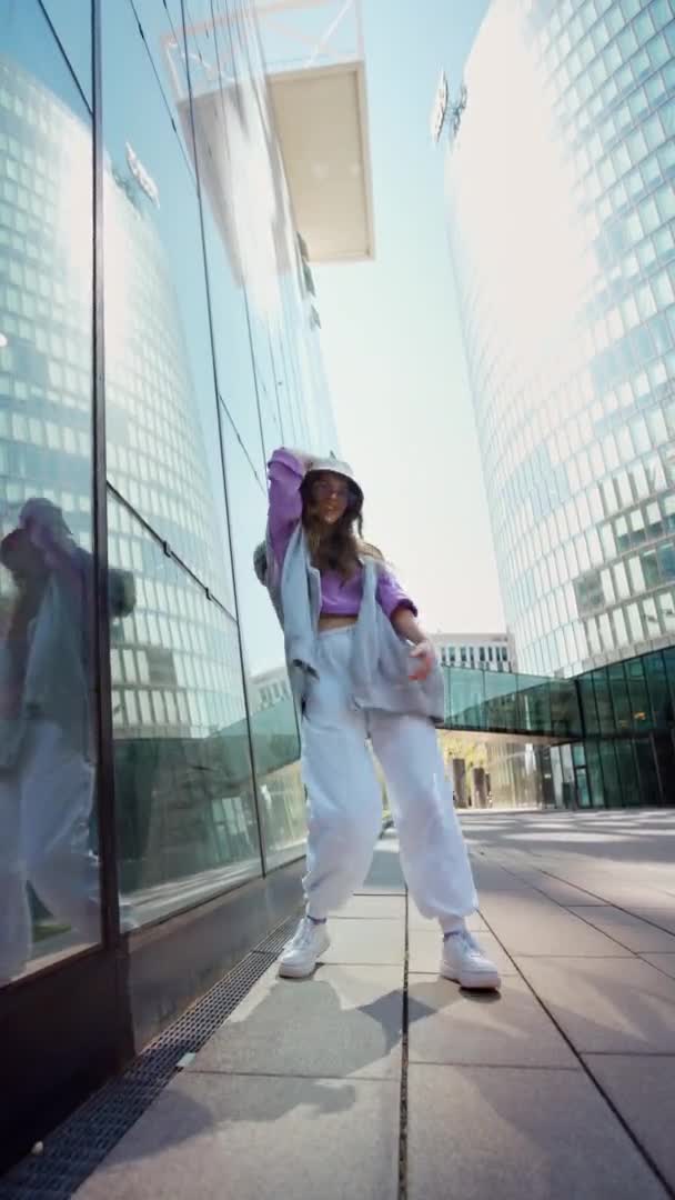 Fashionable funky caucasian girl dancer in sportswear is performing outdoor street dancing motion . Vertical slow motion video. Joyful summer female artist demonstrate choreography in the city. — 비디오