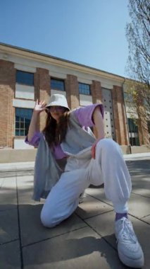 Sokak tarzı giyinmiş hoş bir kız. Kapalı çekim gülümseyen kadın dışarıda kamera için dans ediyor. dikey video. Neşeli kadın, müziğin ritmine ayak uyduruyor.