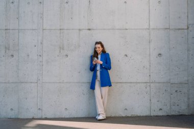 İnternet bankacılığı mobil uygulaması kullanan bir kadın. Düşük ihtimal. Duvarın önünde duruyor. İzole edilmiş arkaplan.