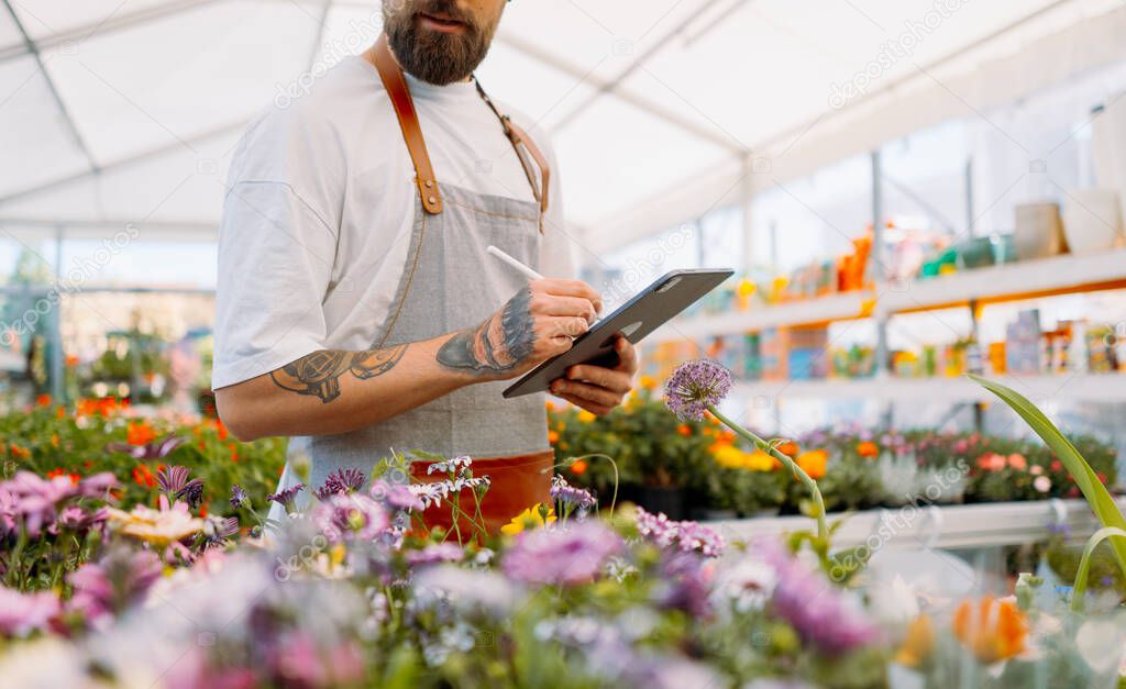 Midsection of gardener using tablet in garden centre.