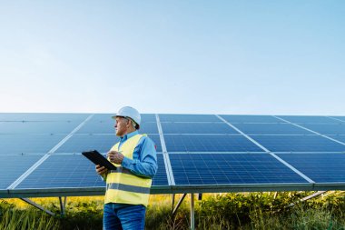 Mühendis güneş panellerinin önünde duruyor. Tableti tutup fotovoltaik güneş panellerini kontrol ediyorum. Yüksek kalite fotoğraf