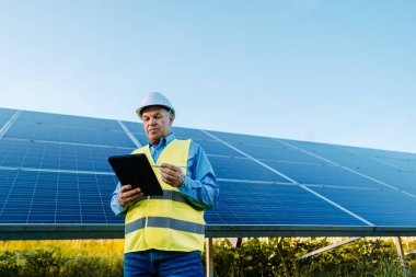Mühendis güneş panellerinin önünde duruyor. Tableti tutup fotovoltaik güneş panellerini kontrol ediyorum. Yüksek kalite fotoğraf
