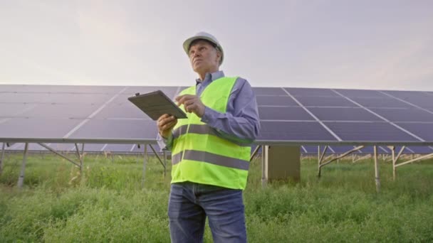 エンジニアは太陽電池パネルの前に立つ タブレットを保持し 太陽電池パネルをチェック — ストック動画