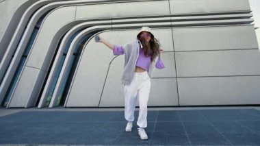Positive girl listening to music and amusingly dancing on a city background. Woman is having fun alone and feeling happy and carefree. Cheerful dance. Entertainment concept. High quality 4k footage