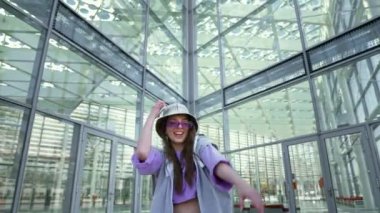 Karizmatik ve heyecanlı bayan dans ediyor ve akıllı telefonundan müzik dinliyor. Sokakta zaferi kutlayan mutlu kadın. Kentsel fütüristik geçmiş. Yüksek kalite 4k görüntü