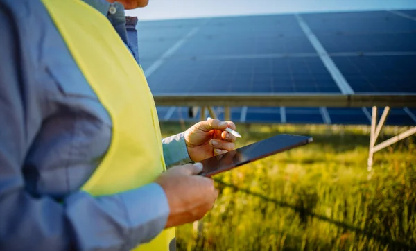 Alternative source of electricity. Inspector engineer man holding digital tablet working in solar panels power farm, photovoltaic cell park. Innovation and green power concept 