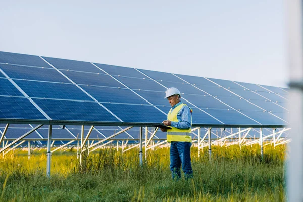 Güneş paneli alanında muayene için yürüyen üniformalı kıdemli mühendis. Ekolojik yapı. Güneş enerjisi santrali. Yeşil enerji kavramı
