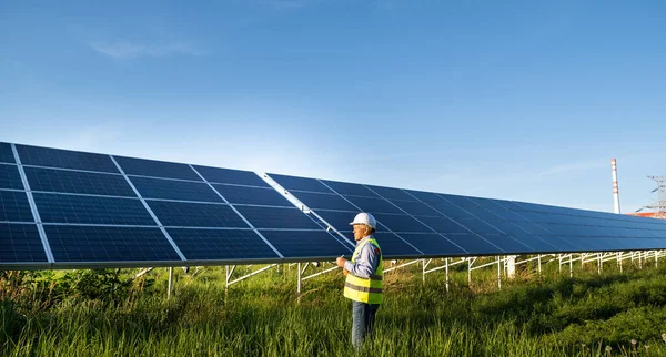 Solar engineer working with digital tablet at renewable energy farm. Male ecological engineer uses folder and collects efficient information about solar panels. Alternative Eco energy concept