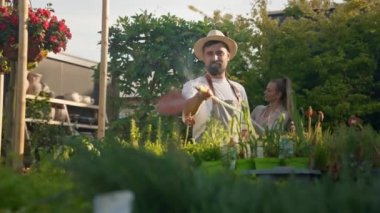 Bahçe merkezinde çalışan iş arkadaşları. Arka plandaki bitkilerle ilgilenen kadın meslektaşı ile birlikte hortumla bahçeyi sulayan erkek bahçıvan. Sera konsepti 