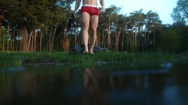 Cropped view of the half naked man throwing his towel and entering frozen lake with ice cold water. Male person sinks into the ice liquid for polar plunge ice swimming. Healthy lifestyle concept