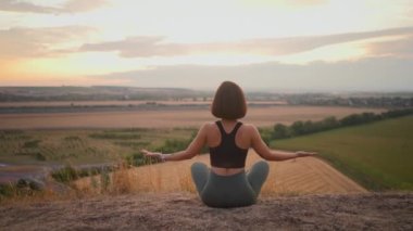 Athletic lady is doing fitness among green wild nature. Woman sitting in the lotus pose and using yoga practices. Relaxing outside concept