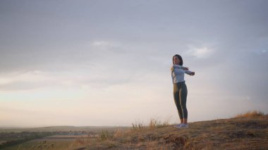 Female trail runner doing a warm-up for her hands on a high mountain. Girl in happy mood during the clear day training at the open air