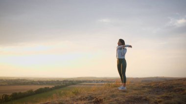 Female trail runner doing a warm-up for her hands on a high mountain. Girl in happy mood during the clear day training at the open air