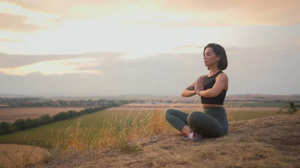 Calm serene sporty young woman meditate while sitting in namaste pose with eyes closed. Girl doing breathing exercises practice while relaxing outdoor