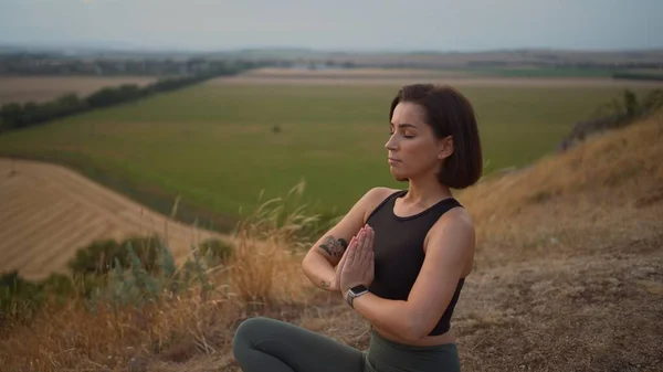 Calm serene sporty young woman meditate while sitting in namaste pose with eyes closed. Girl doing breathing exercises practice while relaxing outdoor