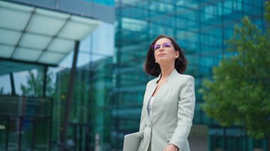 Calm businesswoman looking time on hand watch while going to the work after break. Office worker lady walking through the street in urban city district in morning hour