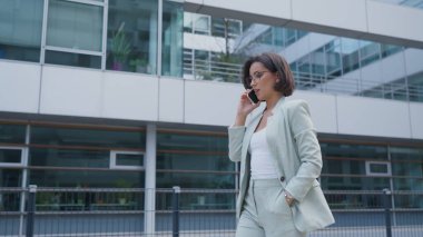 Successful female going to office in modern business center. Beautiful manager talking on a phone, having an Important business call outdoors