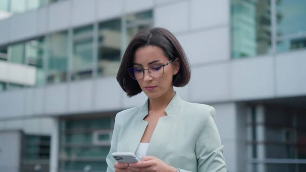 Portrait of independent proud woman with smartphone in her hands walking and answering business emails on an urban background. women leaders concept