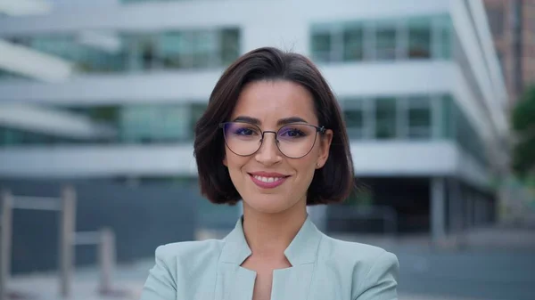 Smiling caucasian young woman in formal outfit looking to camera outside on street while feeling happy. Portrait of business modern manager showing sincere emotions