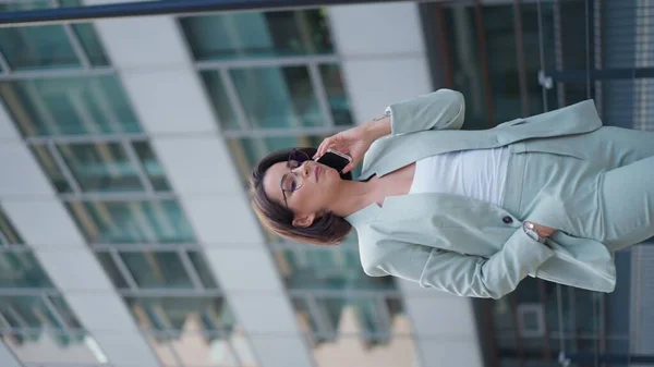 Vertical view of the business woman leadership using smartphone and speaking with client outdoor. Business person dressed green suit talking on cell phone while standing city street
