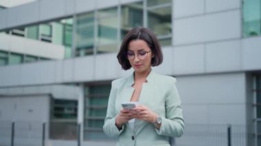Portrait of independent proud woman with smartphone in her hands walking and answering business emails on an urban background. women leaders concept
